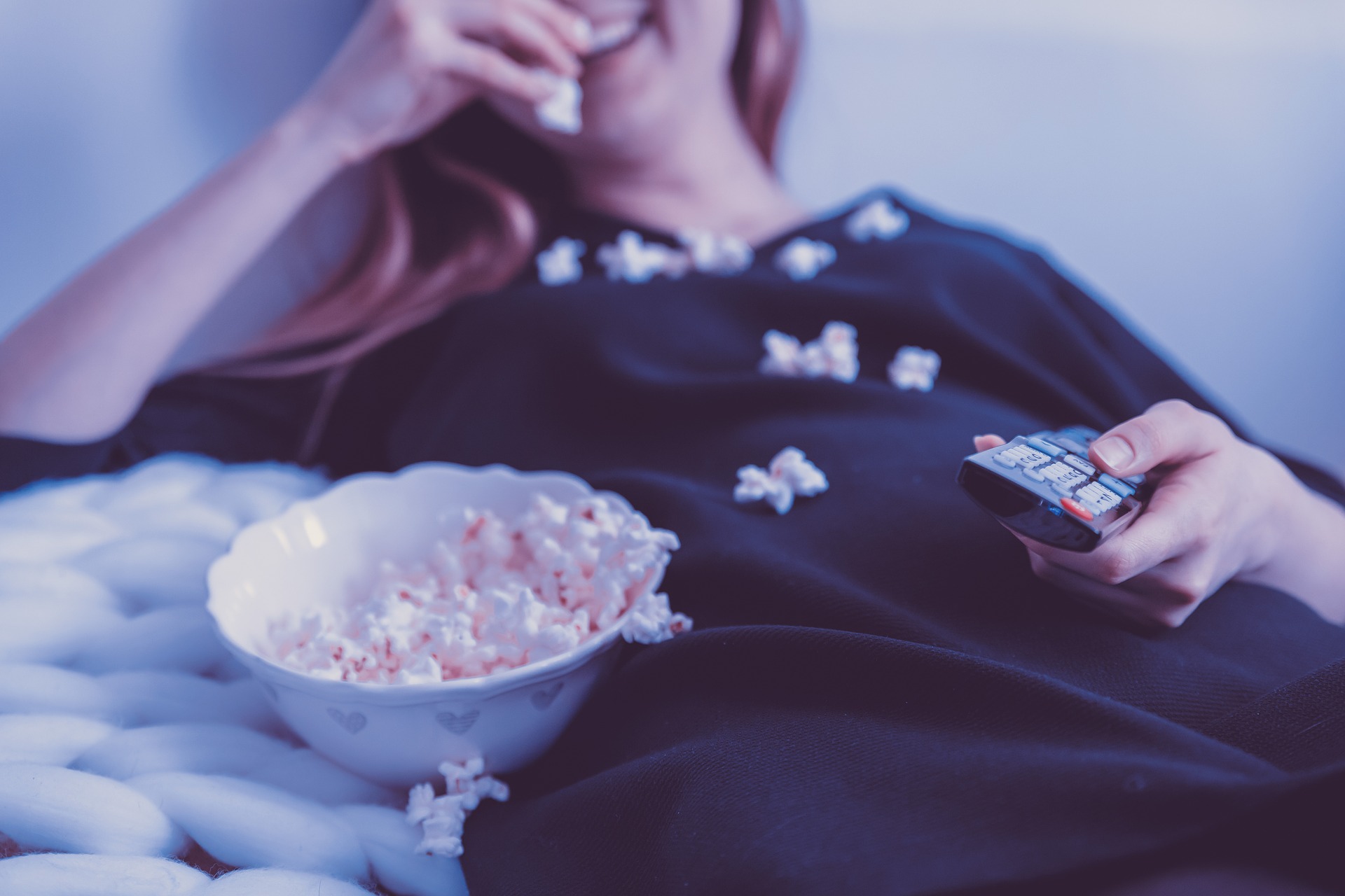 A woman eating popcorn on a couch while watching television.