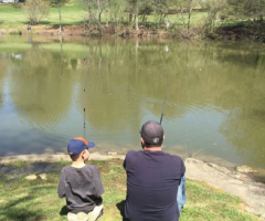 A child and parent fishing on the lakeside.