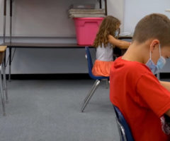 A classroom of children at desks spaced far apart.