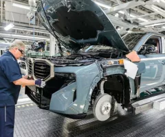 An automotive worker placing a grill on an SUV.